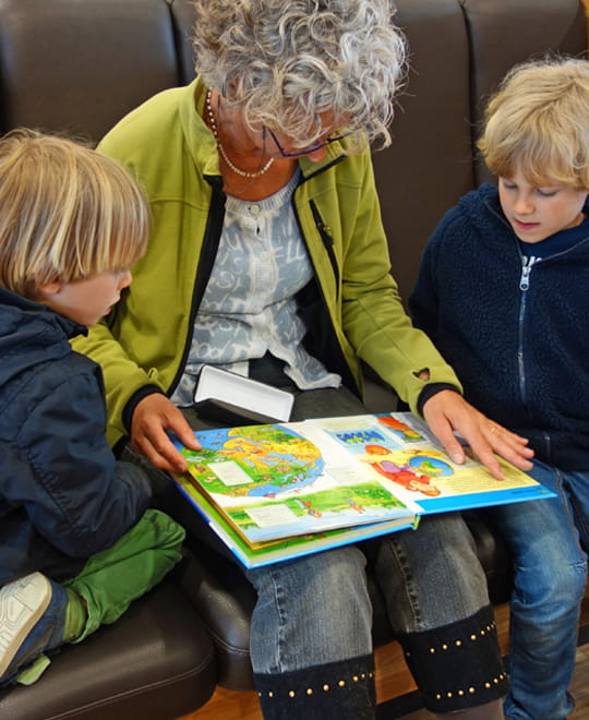 Gemeinsam in einem Kinderbuch lesen Erwachsene Person liest gemeinsam mit zwei Kindern in einem Bilderbuch als Motiv für Kinderbücher und Lesekultur